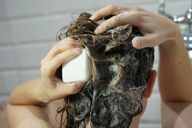 Caucasian woman washes her brown hair with shampoo bar or soap, zero waste concept
